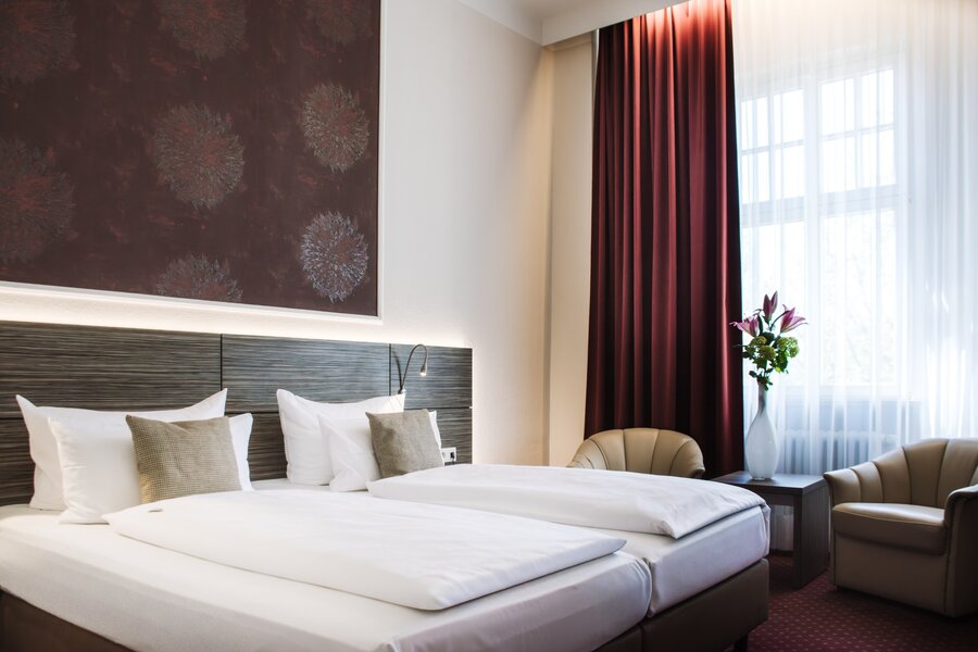 Ein Doppelzimmer mit zwei Einzelbetten, zwei Sesseln und großem Fenster im Hotel Prinzregent.