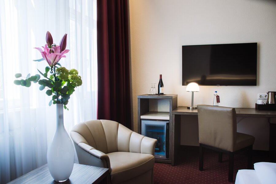 Ein Sitzbereich mit Sessel, kleinem Tisch mit Blumen und Schreibtisch im Doppelzimmer des Hotel Prinzregent.