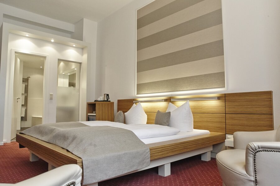 Ein Superior‑Doppelzimmer mit großem Bett, offenem Badbereich und modernem Holzdesign im Hotel Prinzregent.