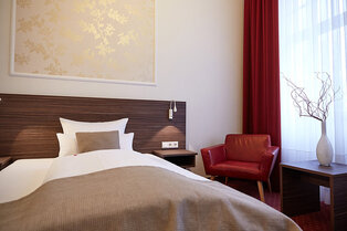 Elegantes Doppelzimmer im Hotel Prinzregent mit einem komfortablen Doppelbett, Kronleuchter und zwei blauen Sesseln.