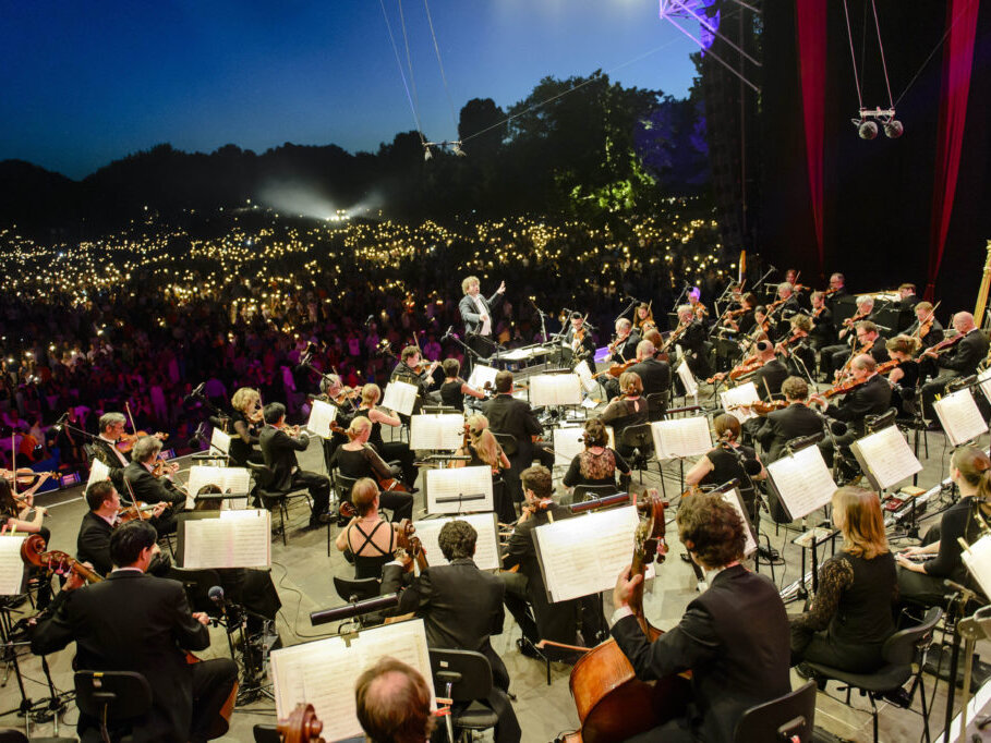 Orchester beim Klassik Open Air in Nürnberg vor einem Publikum mit leuchtenden Lichtern bei Dämmerung.