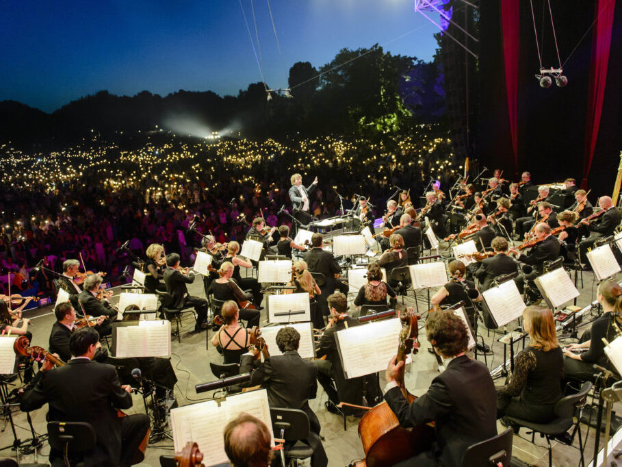 Orchestra performing at the Klassik Open Air in Nuremberg in front of an audience with lights at twilight.