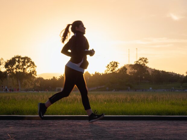 Silhouette einer Frau beim Joggen in einem Park während des Sonnenuntergangs.