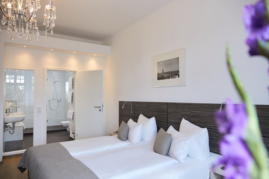 Ein Superior‑Zweibettzimmer mit zwei Einzelbetten, Blick ins Bad und dezenten Blumen im Vordergrund im Hotel Prinzregent.