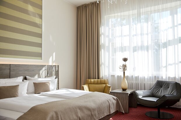 Ein Superior‑Doppelzimmer mit großem Bett, zwei Sesseln, kleinem Tisch mit Deko und hellem Fenster im Hotel Prinzregent.