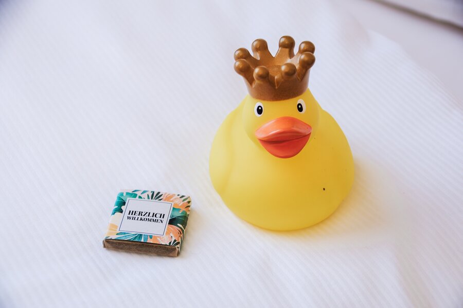Eine gelbe Quietscheente mit Krone und Willkommensschokolade auf weißer Oberfläche im Hotel Prinzregent.