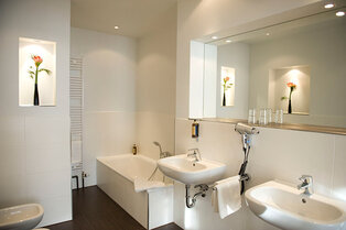 Modernes, helles Badezimmer im Hotel Prinzregent mit zwei Waschbecken und Badewanne.