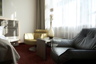 Ein moderner Sitzbereich mit schwarzem Ledersessel, gelbem Stuhl, kleinem Tisch mit Vase und bodenlangen Vorhängen im Hotel Prinzregent.
