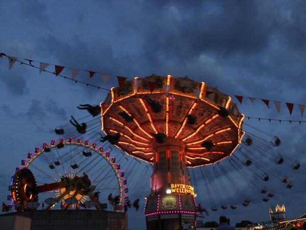Illuminated chain carousel and Ferris wheel at the Nuremberg Volksfest at twilight.