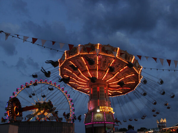 Beleuchtetes Kettenkarussell und Riesenrad auf dem Nürnberger Volksfest bei Dämmerung.