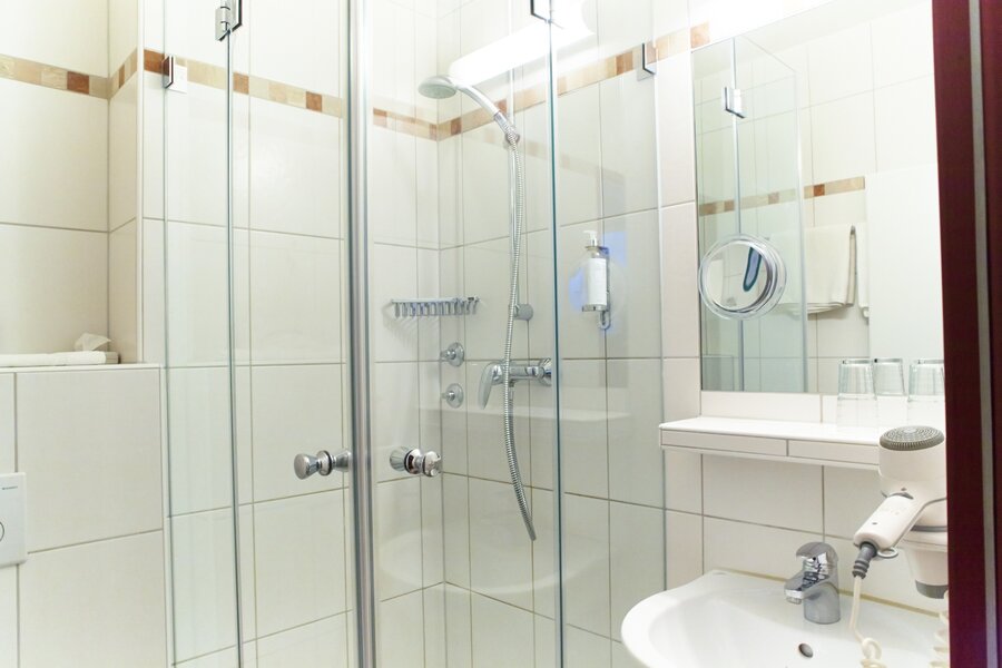 Ein modernes Bad mit Glasdusche, Waschbecken und Föhn im Hotel Prinzregent.