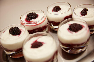Sechs Dessertgläser mit Beerenkompott, heller Creme und je einer Brombeere auf einem Tablett im Hotel Prinzregent.