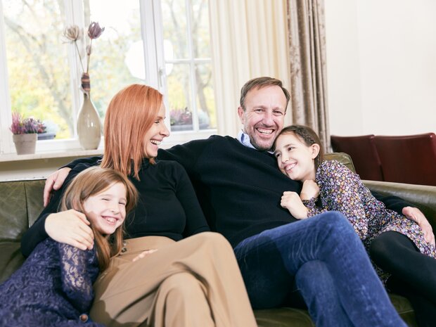 Eine glückliche Familie, bestehend aus Eltern und zwei Töchtern, kuschelt gemeinsam auf einer Couch im Hotel Prinzregent.