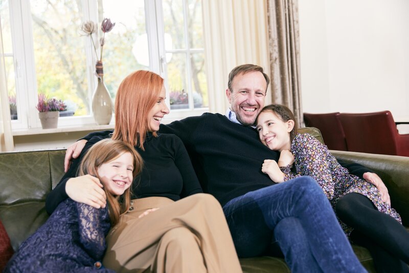 Eine glückliche Familie, bestehend aus Eltern und zwei Töchtern, kuschelt gemeinsam auf einer Couch im Hotel Prinzregent.