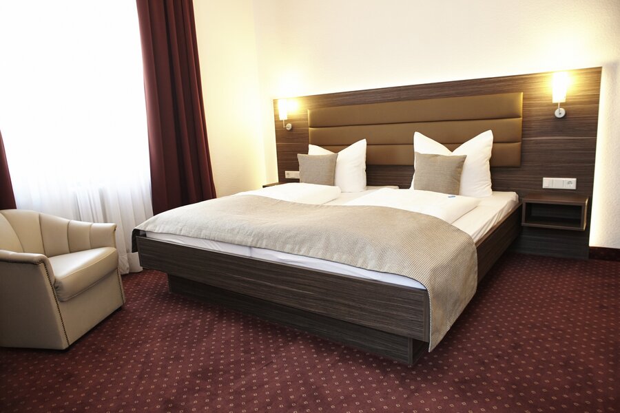 Ein modernes Doppelzimmer mit großem Bett, Sessel und Fenster im Hotel Prinzregent.