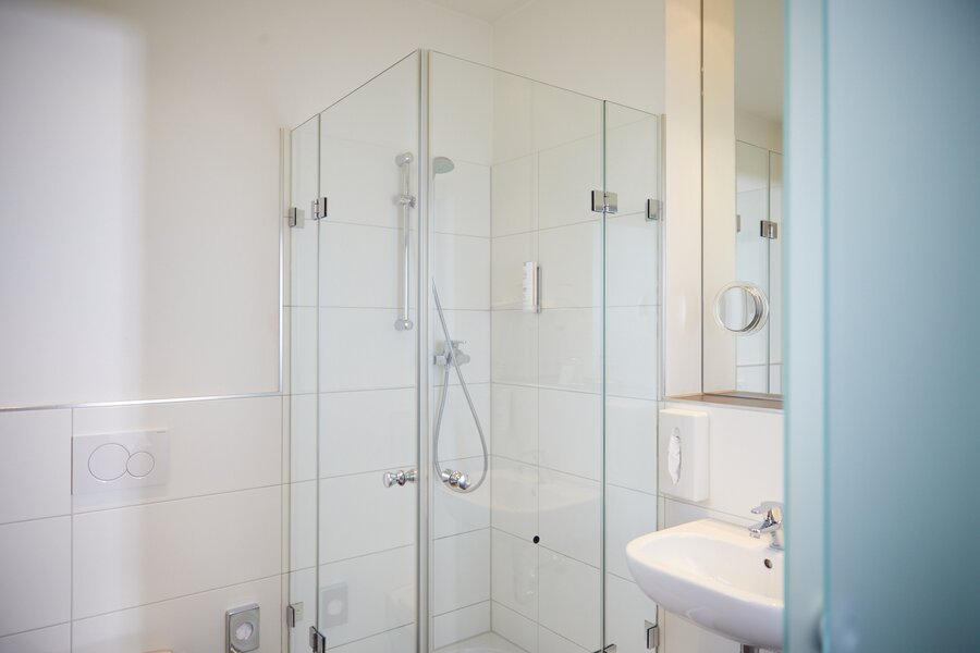 Ein modernes Bad mit Glasdusche, Waschbecken und weißen Fliesen im Hotel Prinzregent.