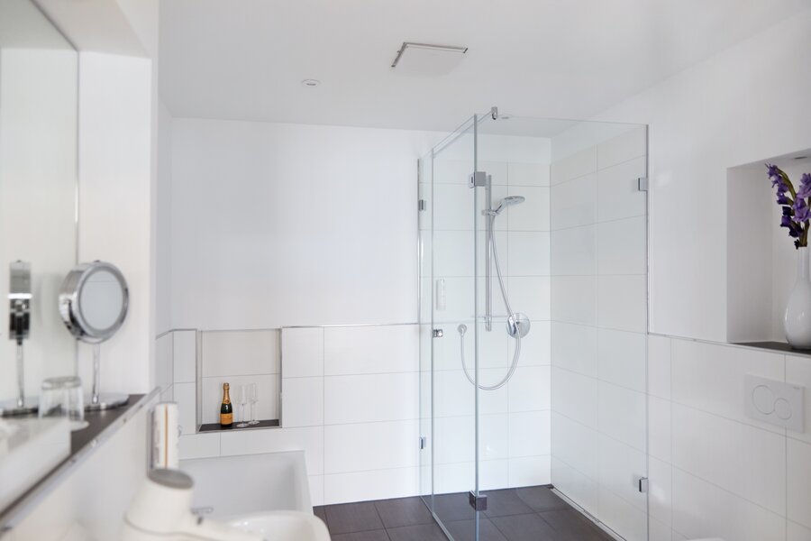 Ein modernes Superior‑Bad mit Glasdusche, Waschbecken, Föhn und dekorativer Blumennische im Hotel Prinzregent.