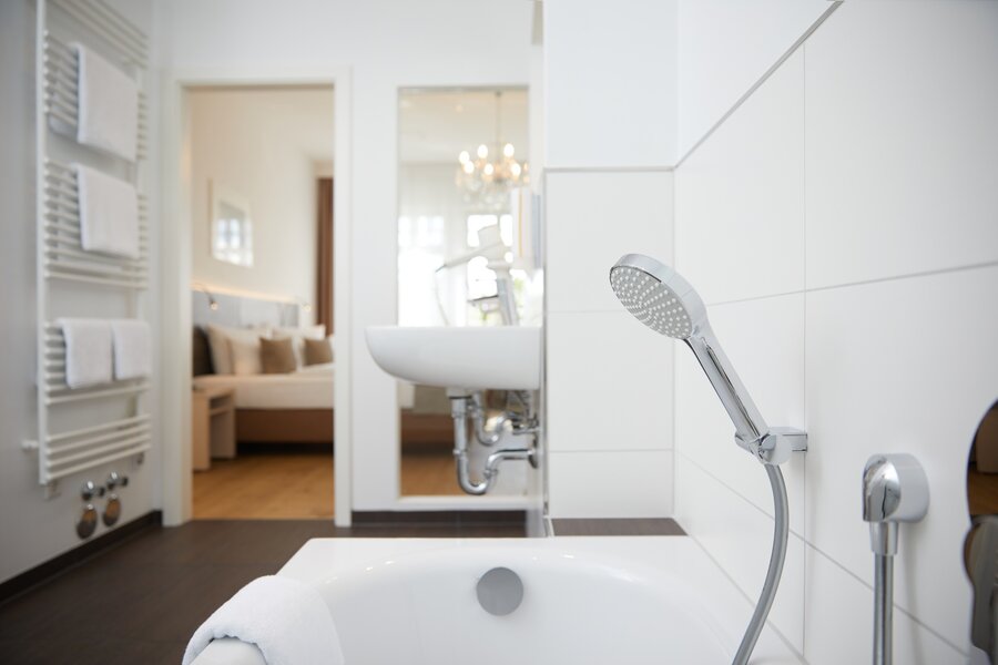 Ein Superior‑Bad mit Badewanne, Handtuchwärmer, Waschbecken und Blick ins Schlafzimmer im Hotel Prinzregent.