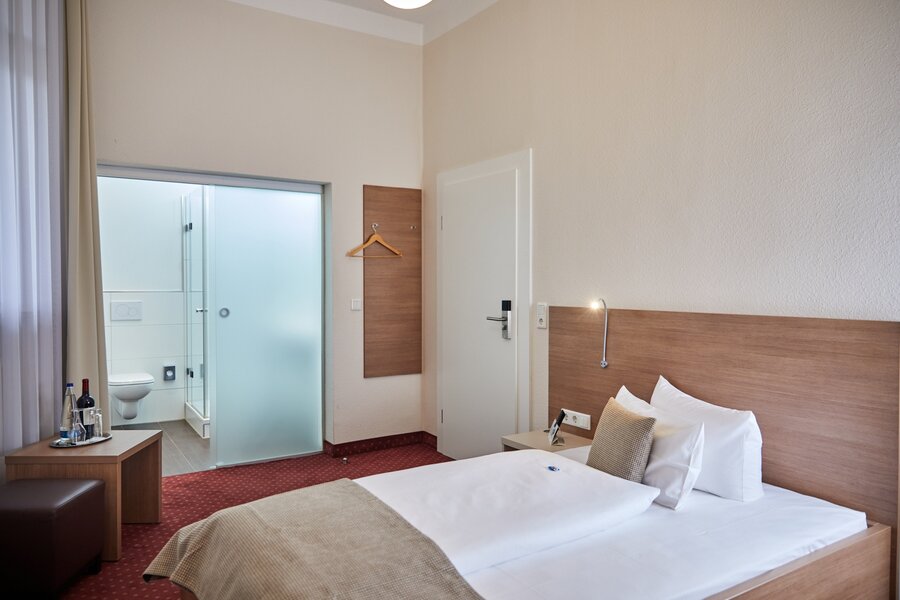 Ein modernes Einzelzimmer mit Bett, kleinem Tisch mit Getränken und Blick ins Bad im Hotel Prinzregent.