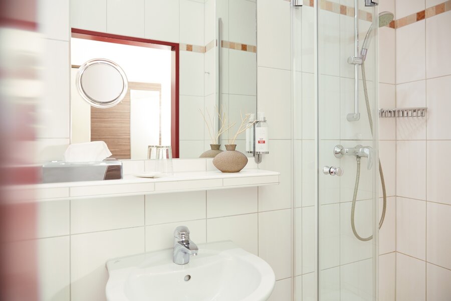 Ein modernes Bad mit Glasdusche, Waschbecken und Ablage mit Deko im Hotel Prinzregent.