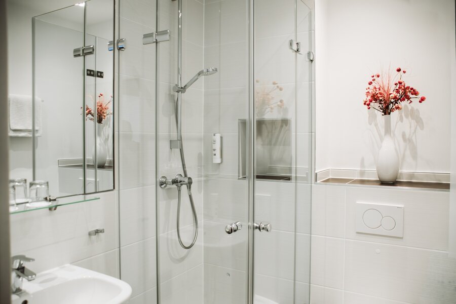    Ein modernes Bad mit Glasdusche, Waschbecken und Deko‑Blumen im Hotel Prinzregent.
