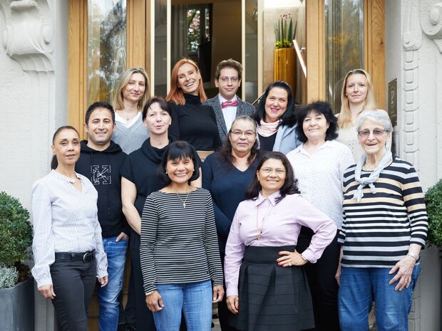 Eine Gruppe von dreizehn Personen steht für ein Gruppenfoto vor einem Gebäude mit Holztüren und großen Pflanzkübeln.