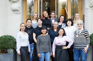 Eine Gruppe von dreizehn Personen steht für ein Gruppenfoto vor einem Gebäude mit Holztüren und großen Pflanzkübeln.