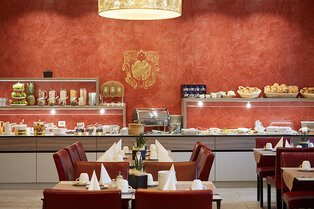 Frühstücksbereich im Hotel Prinzregent mit reichhaltigem Buffet vor einer markanten roten Wand.