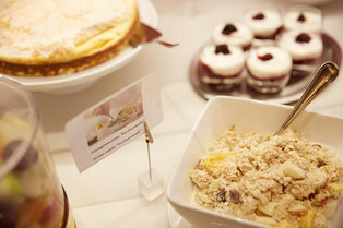 Eine Schale hausgemachtes Birchermüsli mit Löffel, dahinter kleine Dessertgläser und ein Kuchen im Hotel Prinzregent.