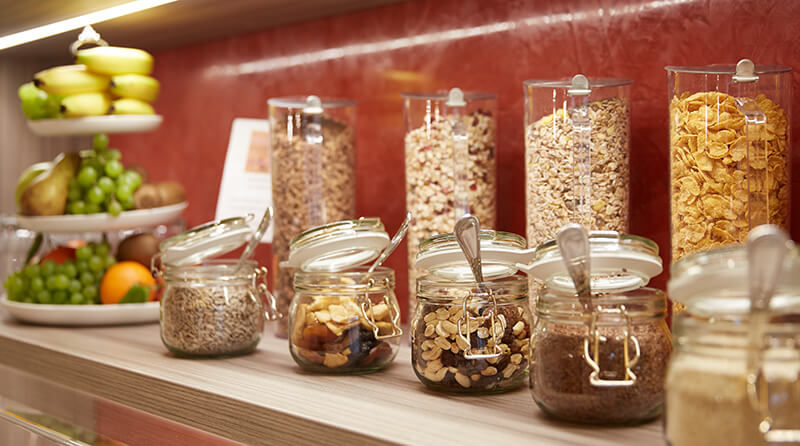 Ein Frühstücksbuffet mit Müslispendern, Gläsern mit Nüssen und Trockenfrüchten sowie einem Obstständer im Hotel Prinzregent.